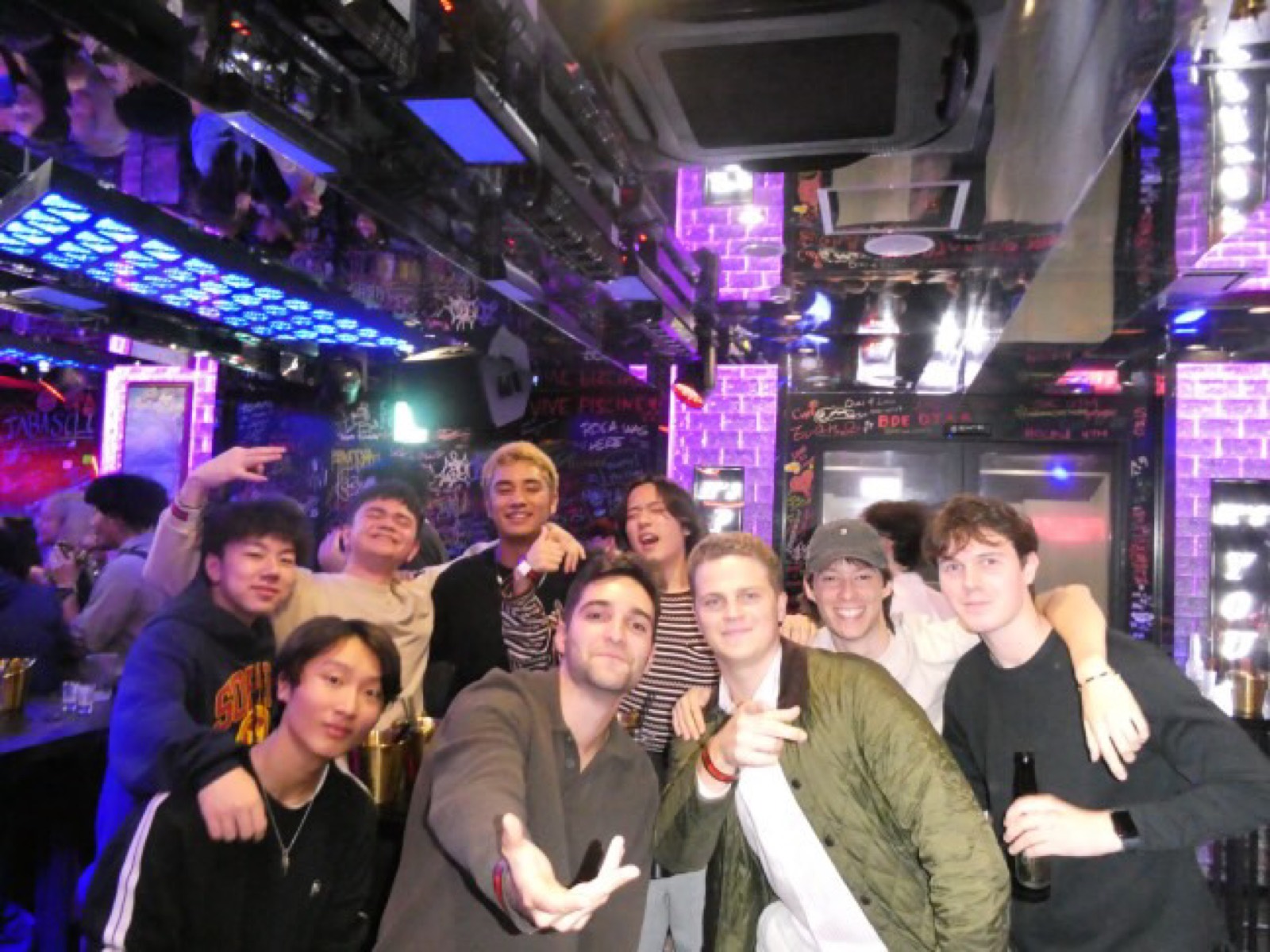 紫とブルーの照明の中、肩を組んでポーズをとる学生グループ — A group of students posing arm in arm under purple and blue club lights