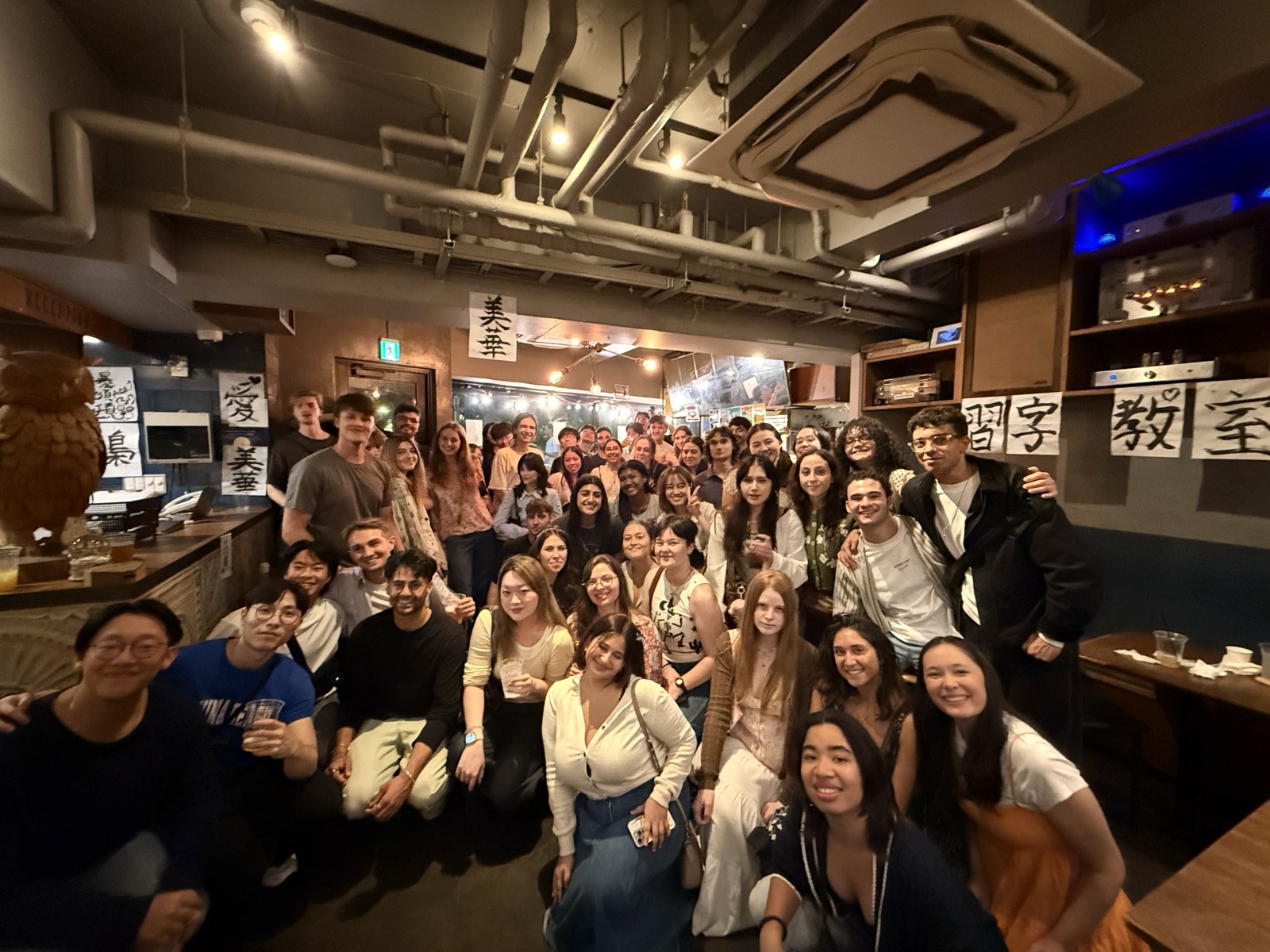 ミートアップ会場で笑顔の集合写真を撮る大勢の学生たち / A big group of smiling students posing together at a meetup