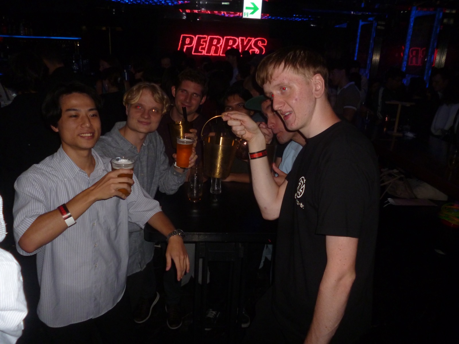 Perry's Bar の赤いネオンサインの前でグラスを掲げる参加者 — Guests raising their drinks in front of the red Perry's neon sign
