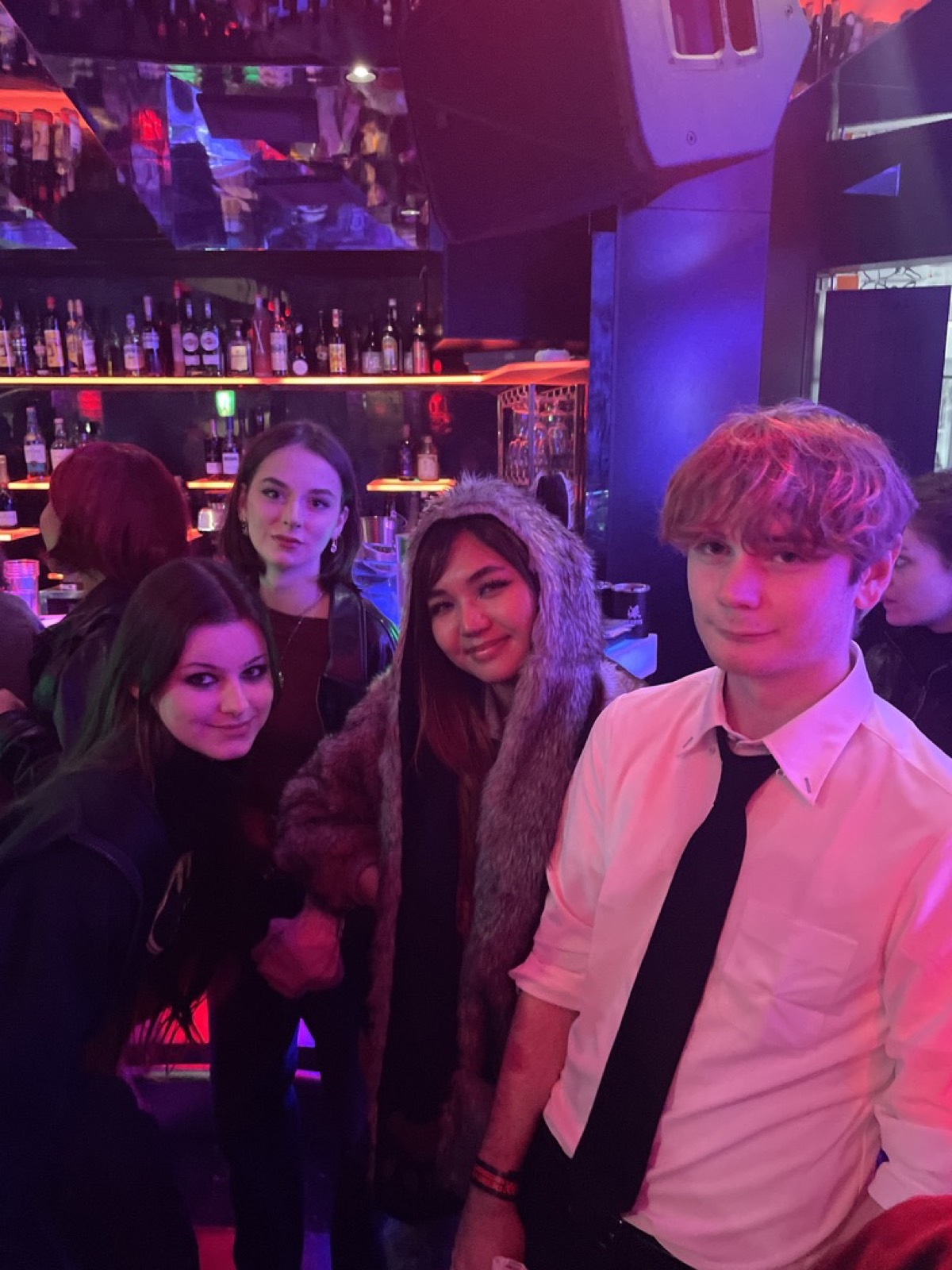 バーカウンターの前でカメラに笑いかける4人の学生 / Four students smiling at the camera by the bar counter